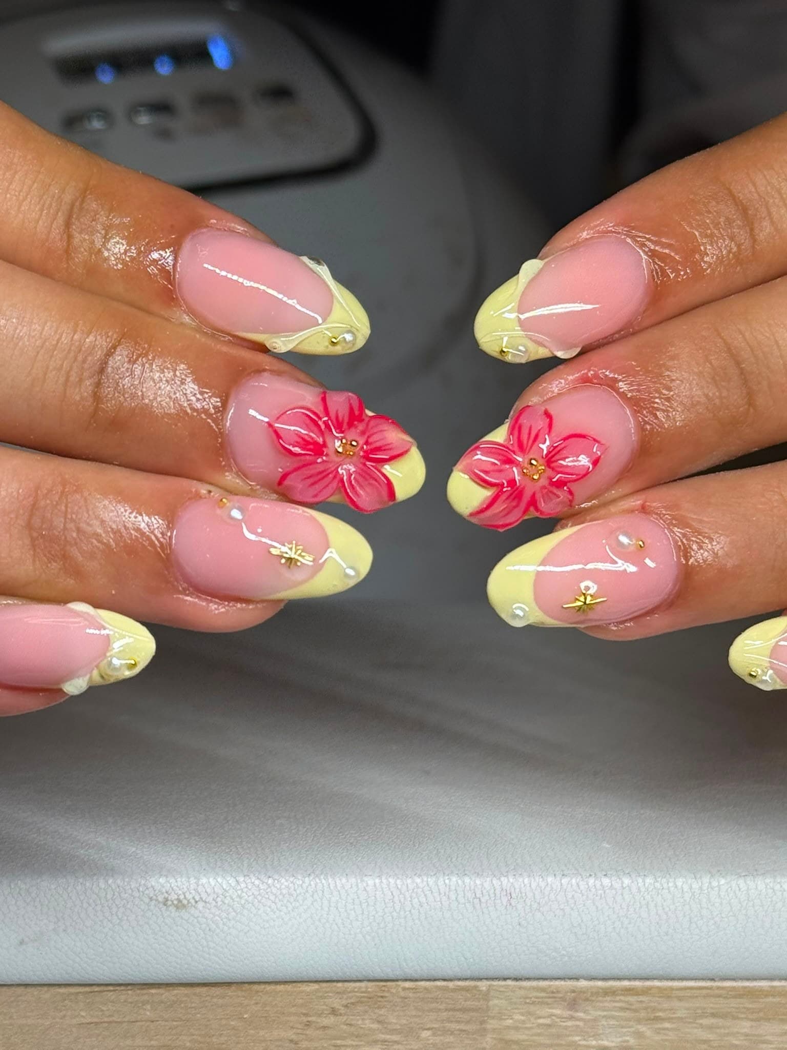 Gele french tips met een handgemaakte rode 3D-bloem, parels en gouden accenten